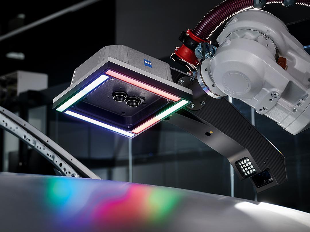 Un braccio robotico dotato di un sensore di scansione 3D ZEISS si estende su una superficie metallica, illuminata da luci LED multicolori.