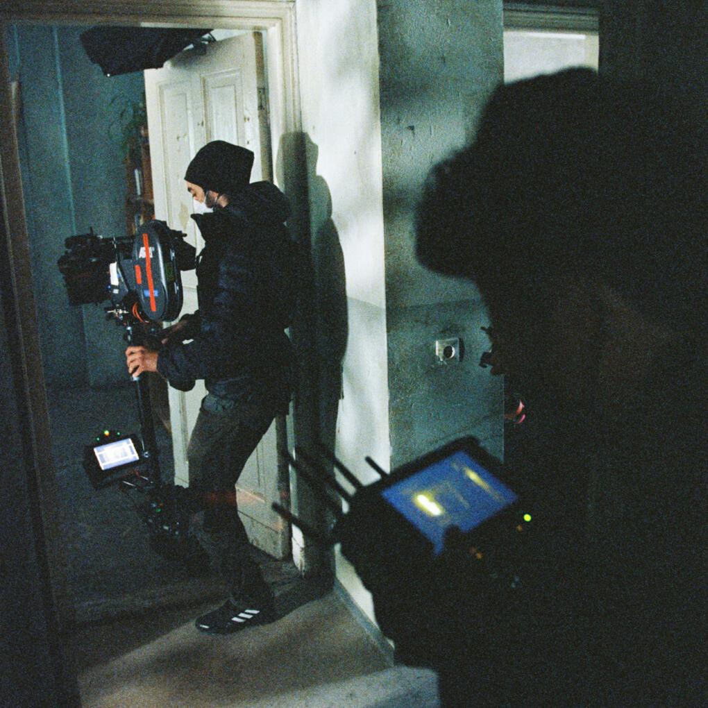 A film crew operates a camera rig and monitor in a dimly lit hallway, capturing a scene with ZEISS cinema lenses.