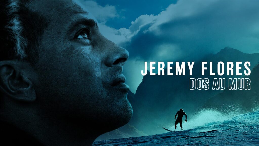 Close-up of a man looking thoughtfully into the distance with ocean waves, mountains, and a surfer in the background, accompanied by the text "JEREMY FLORES DOS AU MUR".