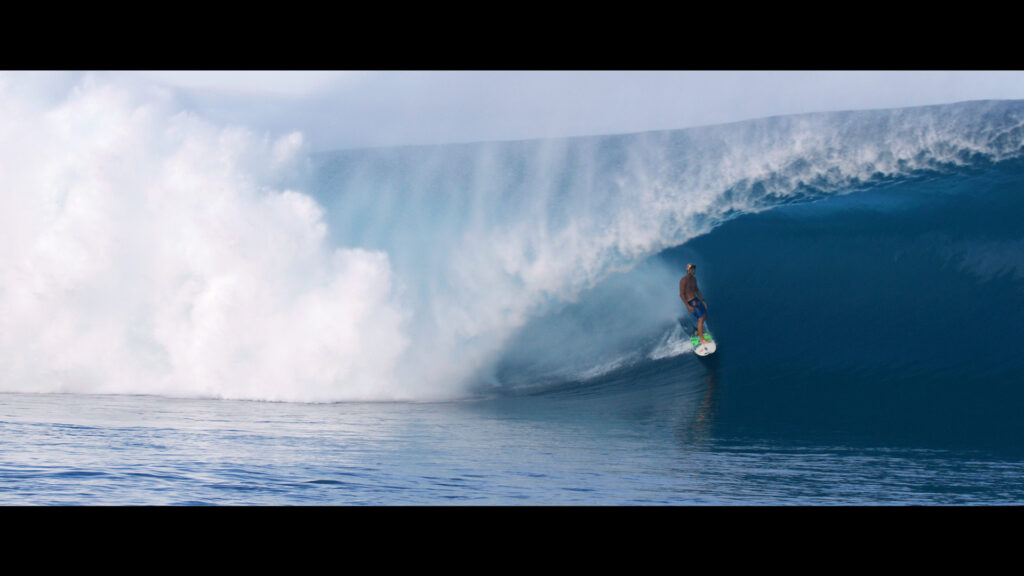 A surfer rides inside the barrel of a large wave with mist and water spray surrounding him.