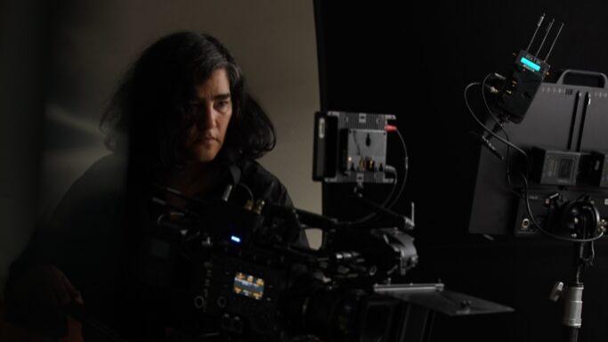 A camera operator films a scene using a professional camera setup equipped with ZEISS lenses in a studio environment.