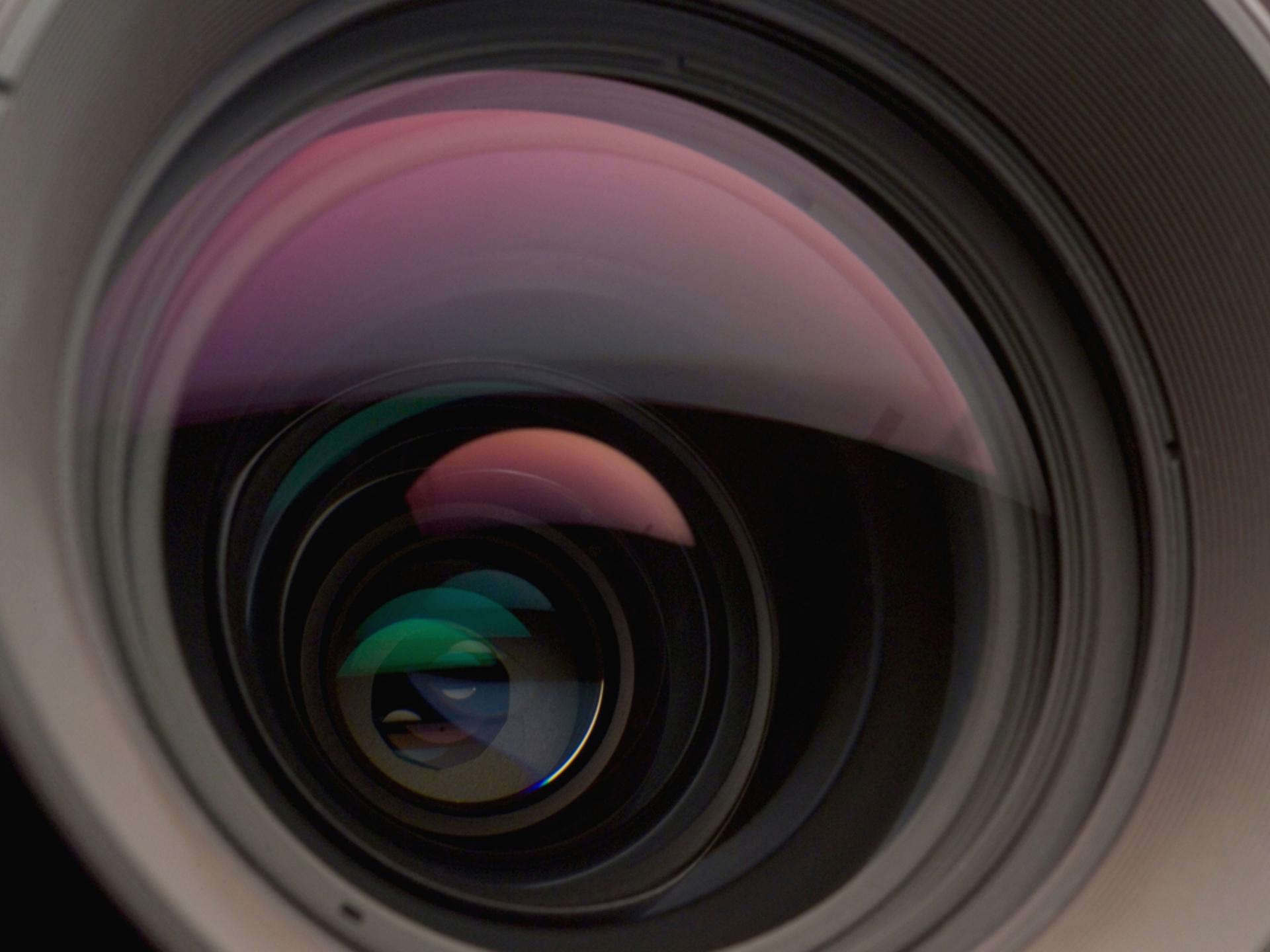 Close-up view of a high-quality ZEISS camera lens showing multiple glass elements and reflections.