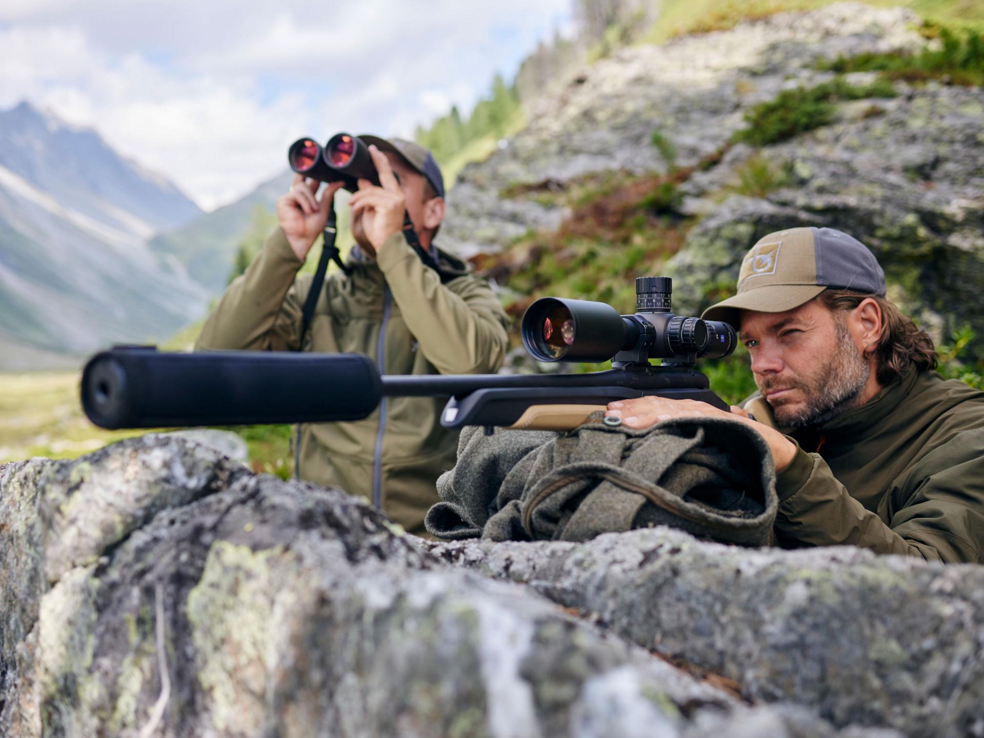 Two hunters in the mountains, one spotting with binoculars and the other aiming through a ZEISS LRP S3 riflescope, ensuring precision and clarity for a successful hunt.