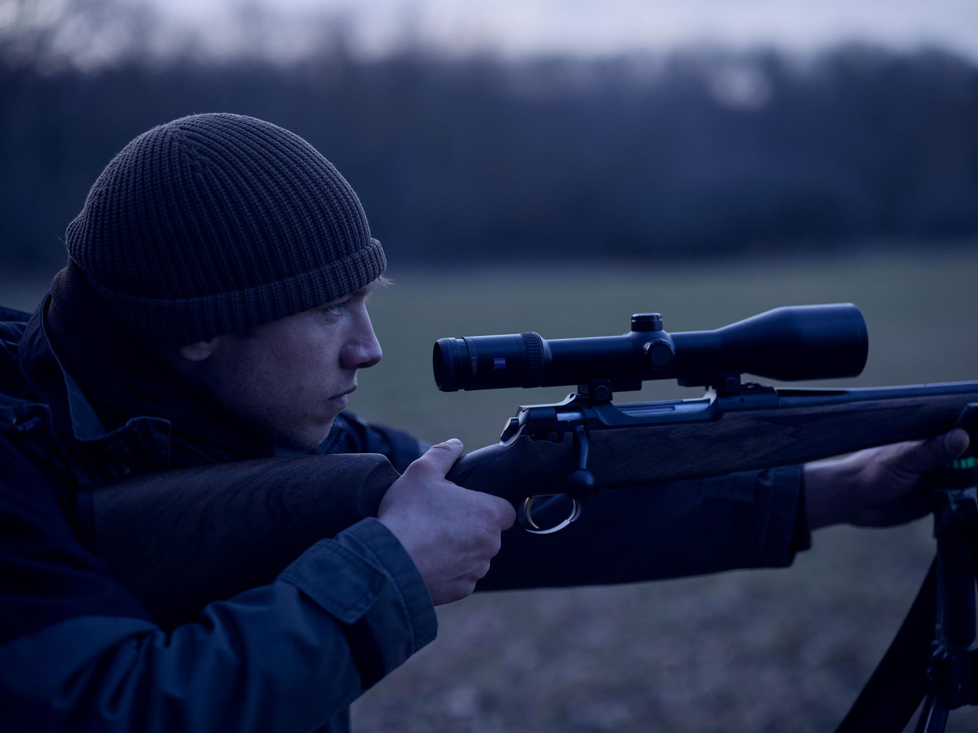 A hunter aims with a ZEISS Victory HT riflescope in low light conditions, highlighting unmatched brightness and high light transmission for reliable performance at dusk.