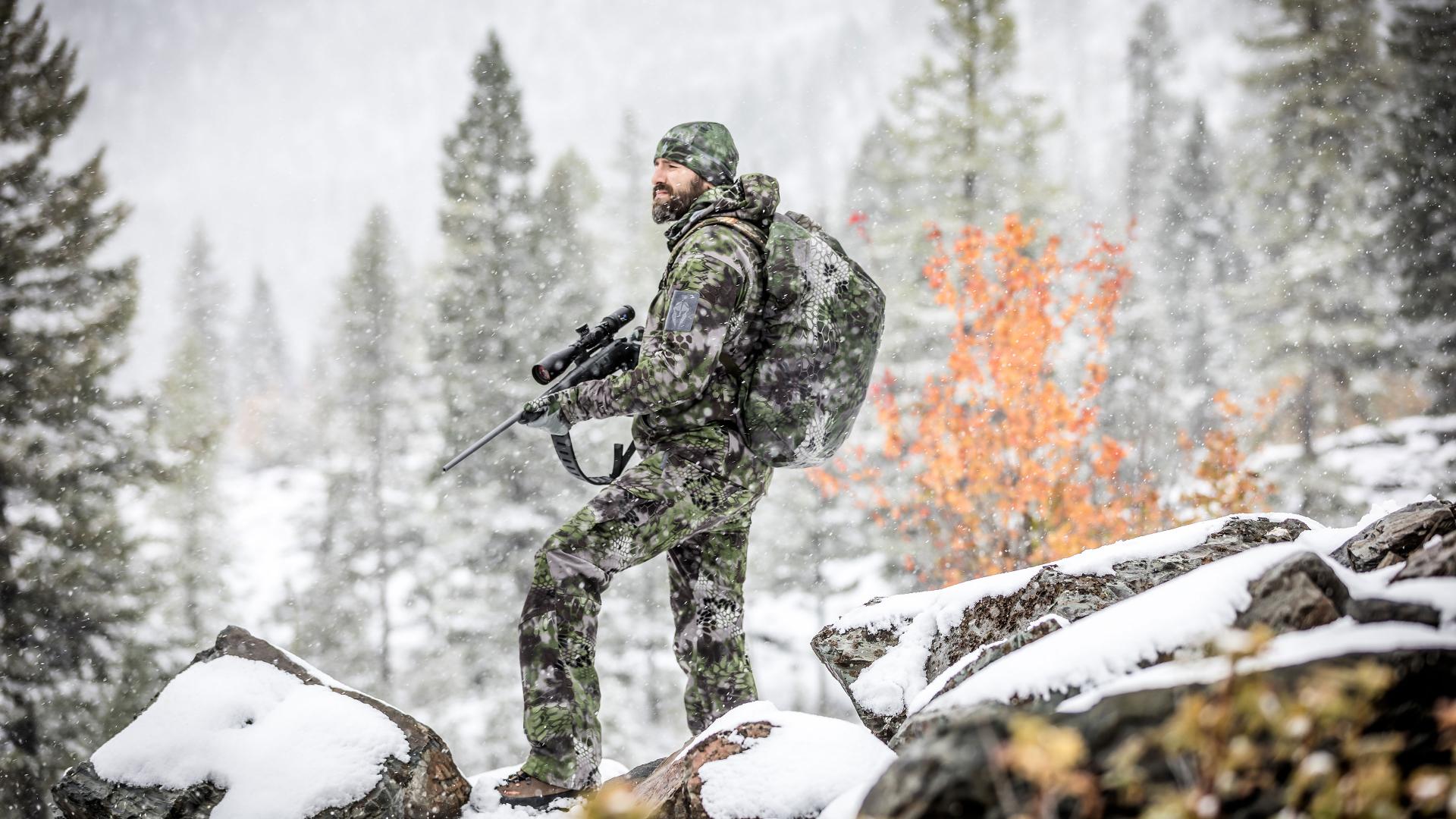 Hunter trekking through snowy terrain with a rifle, demonstrating ZEISS LotuTec® lens coating for clear vision in any weather conditions.