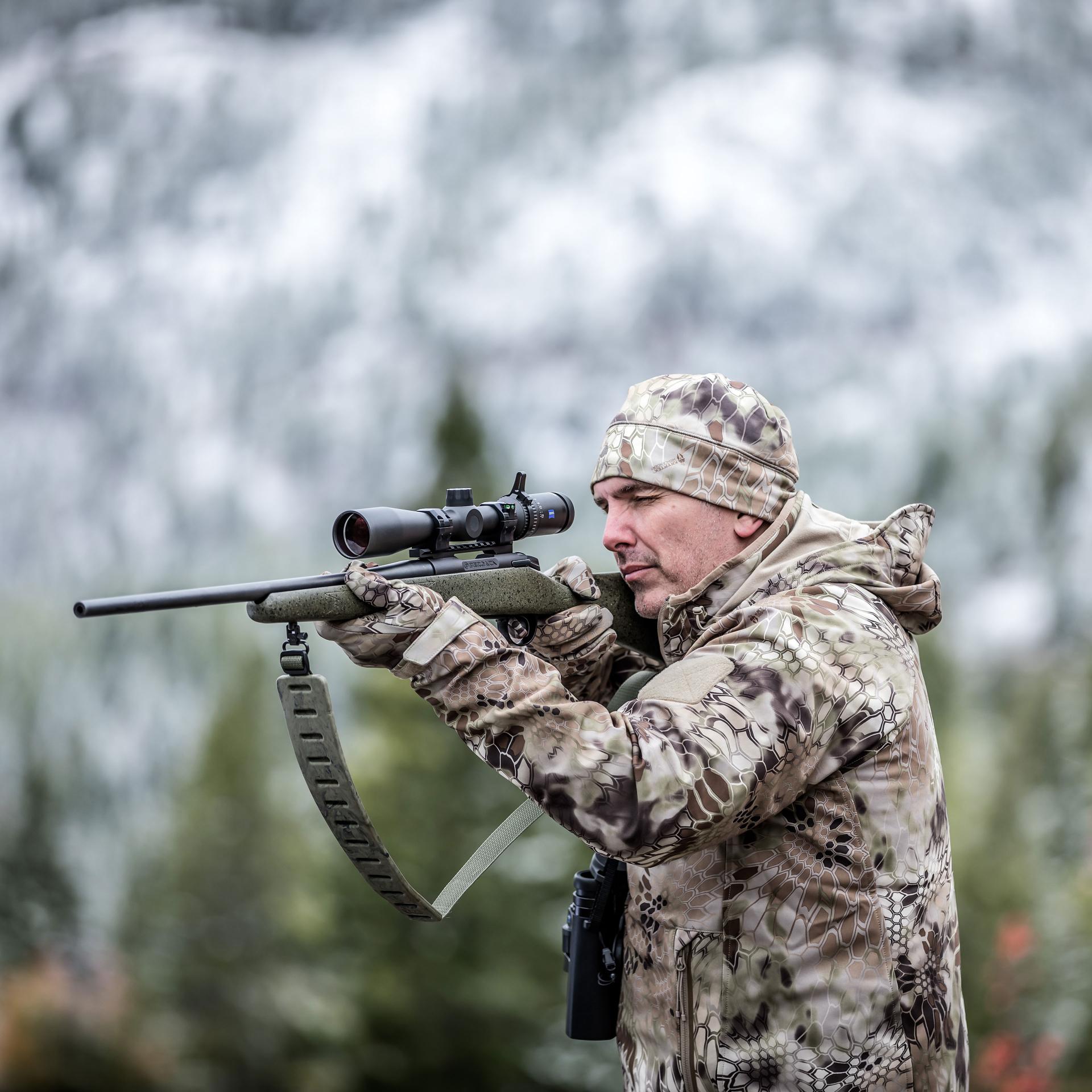 Hunter in camouflage aiming with a rifle fitted with a ZEISS Conquest V4 3-12x56 riflescope, optimized for high-seat hunting and accuracy in low light conditions
