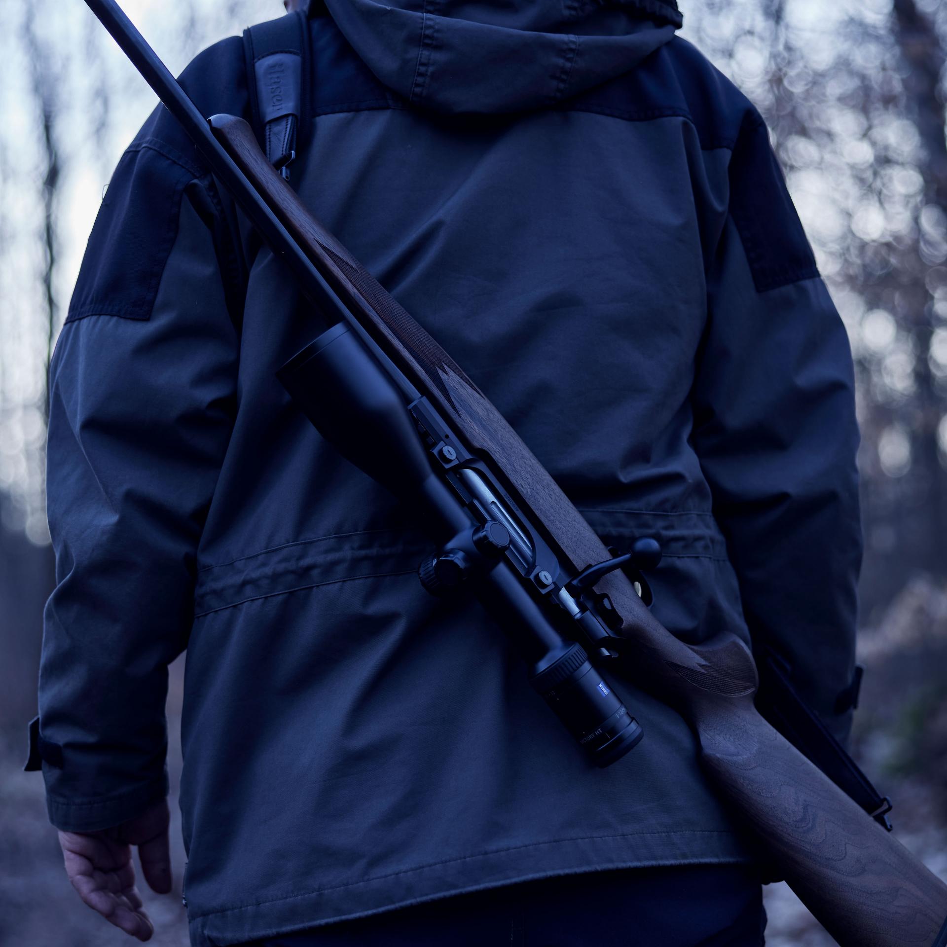 Back view of a hunter carrying a rifle with ZEISS Victory HT 3-12x56 riflescope mounted, emphasizing precision and confidence in low-light hunts.