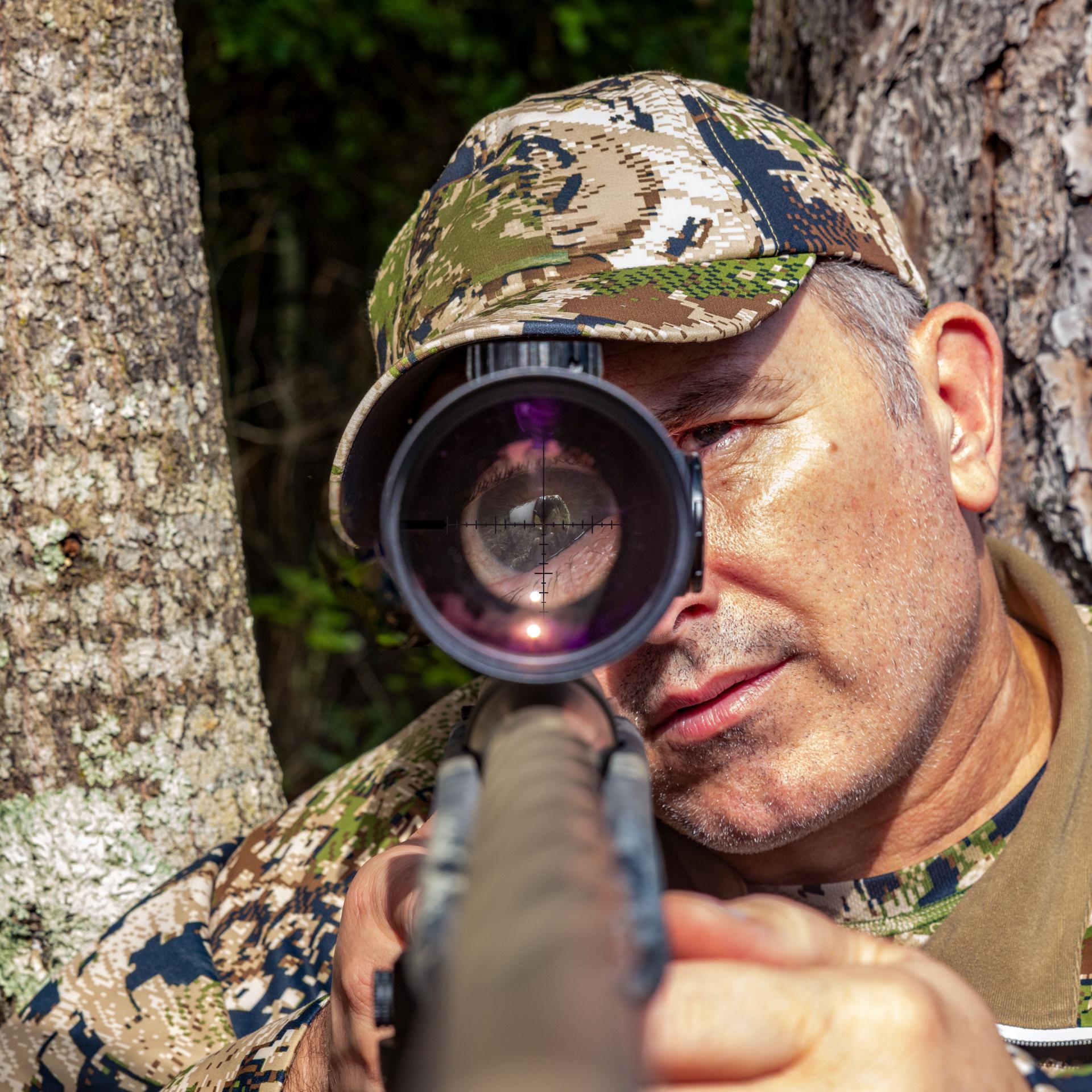 Hunter in camouflage aiming through a rifle equipped with a ZEISS Conquest V6 riflescope, focusing on reticle precision.