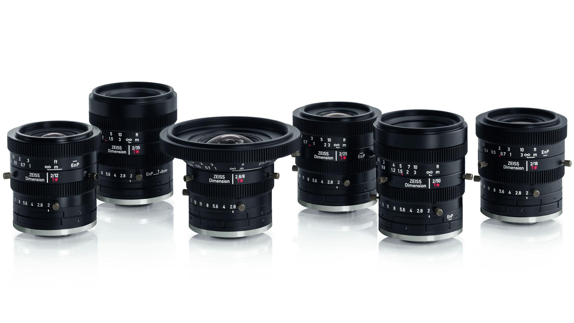 Six ZEISS camera lenses of varying focal lengths are arranged in a row on a white reflective surface.