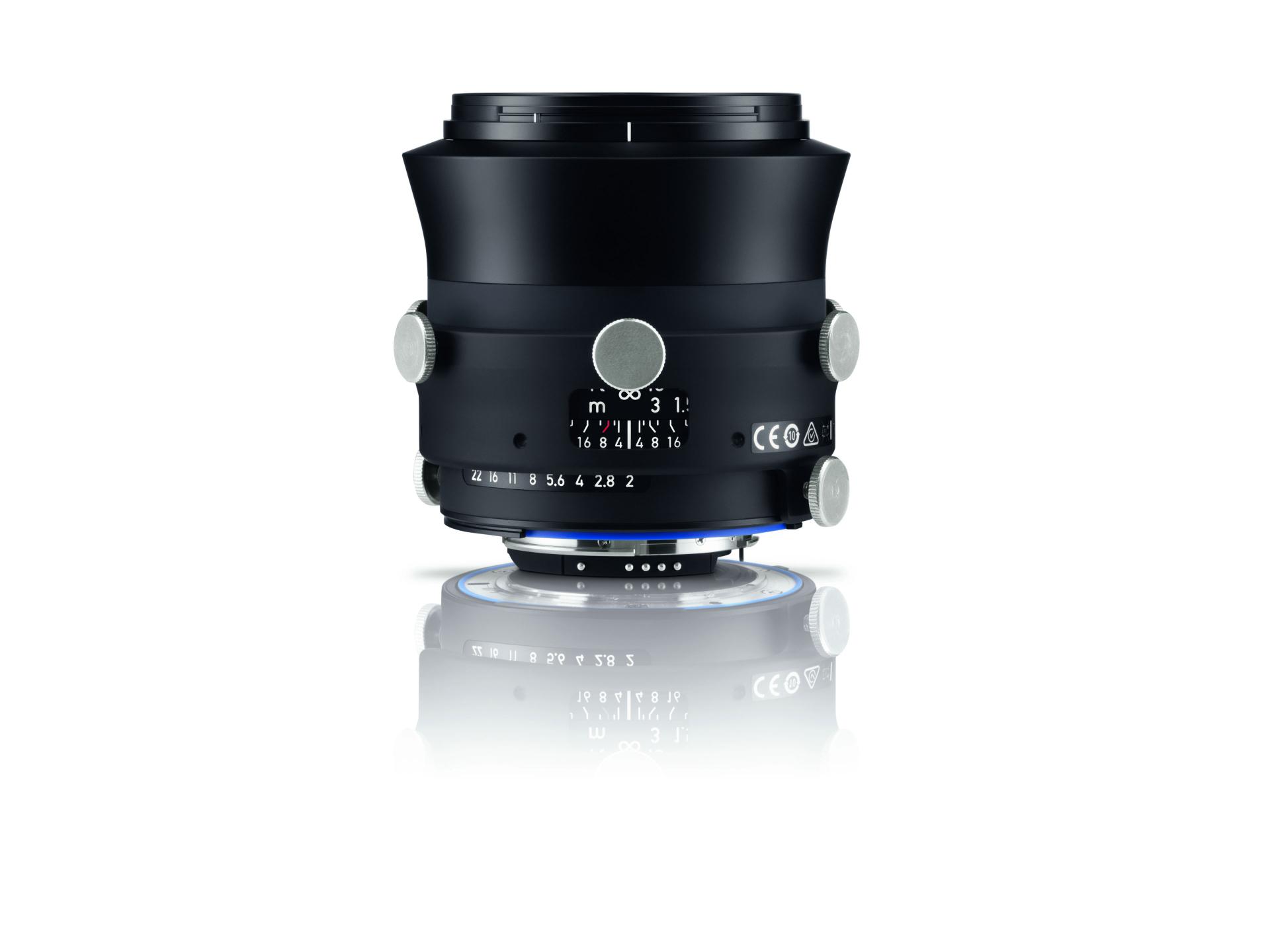 Black ZEISS camera lens with manual focus and aperture markings, featuring silver adjustment knobs, displayed on a reflective white surface.
