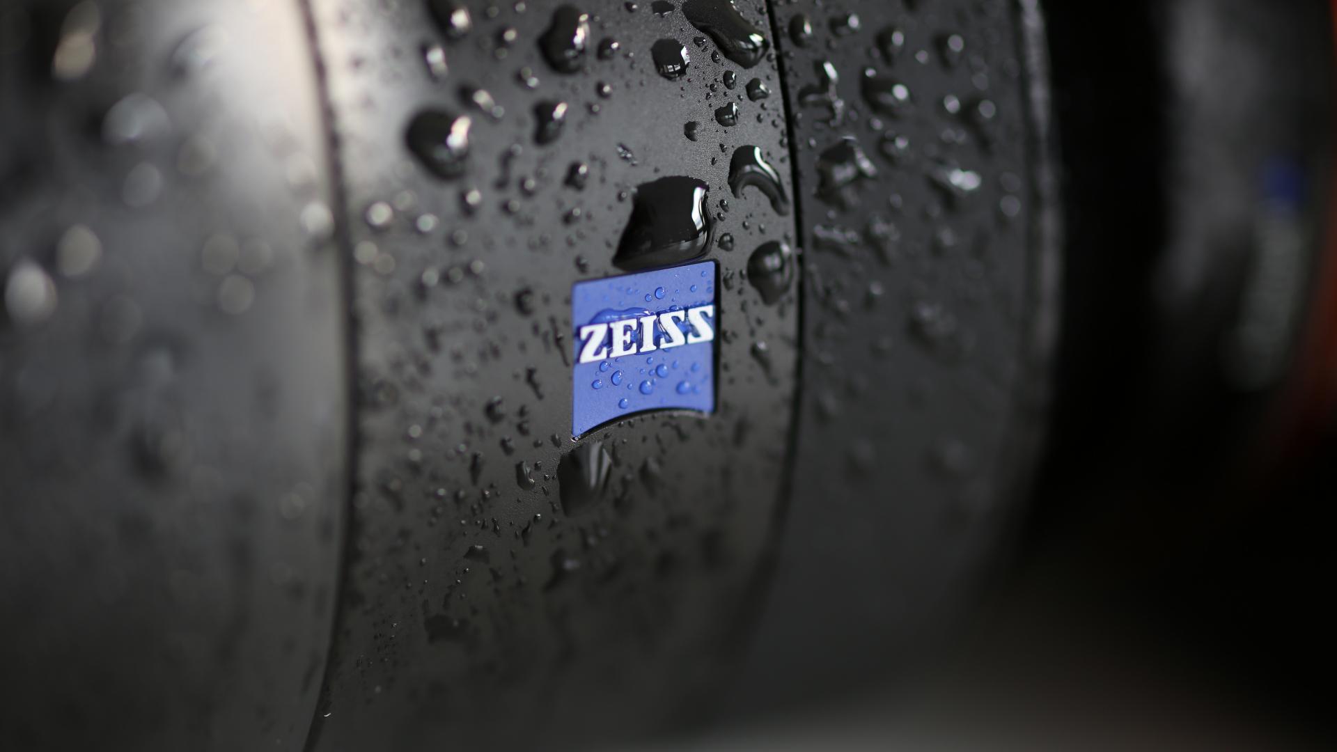 Close-up of a ZEISS camera lens with water droplets on its surface.