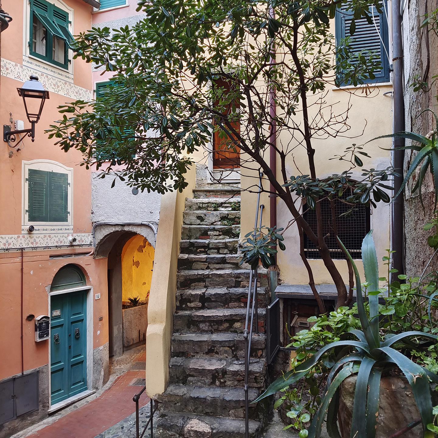 Stone staircase surrounded by colorful buildings and lush greenery in a quaint European alleyway, captured with crisp detail and vibrant colors by a ZEISS camera.