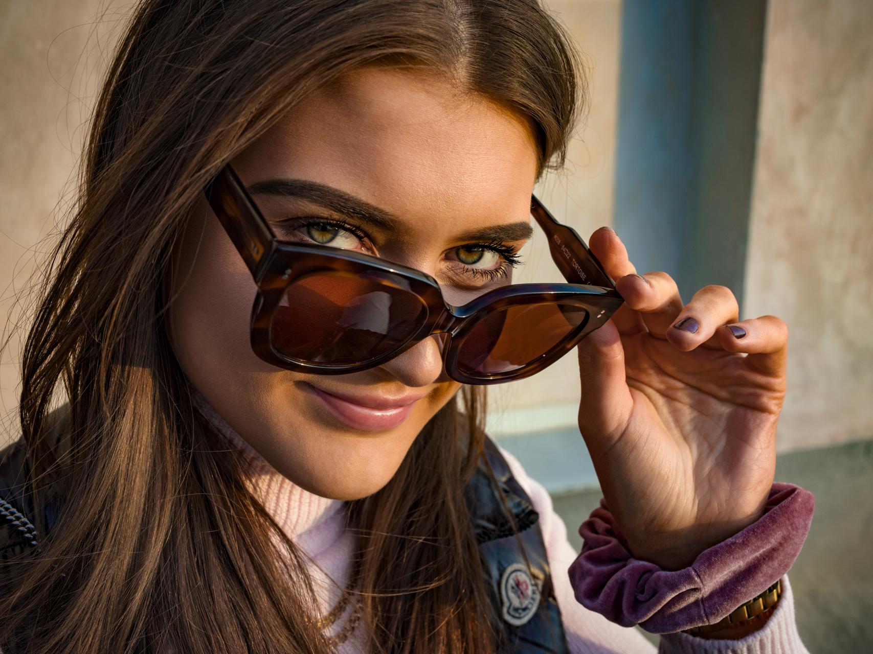 Woman smiling and looking into the camera while adjusting her sunglasses with ZEISS lenses.