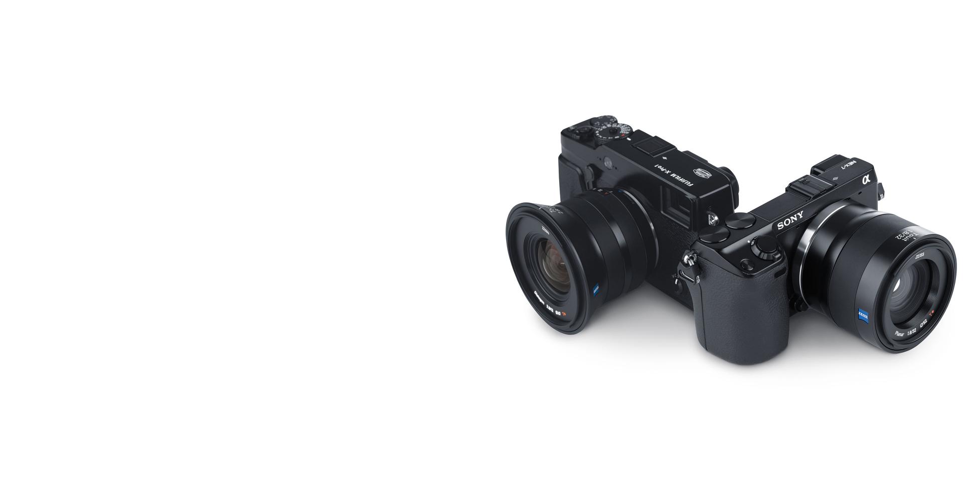 Two black mirrorless cameras equipped with ZEISS lenses are positioned side by side on a white background.