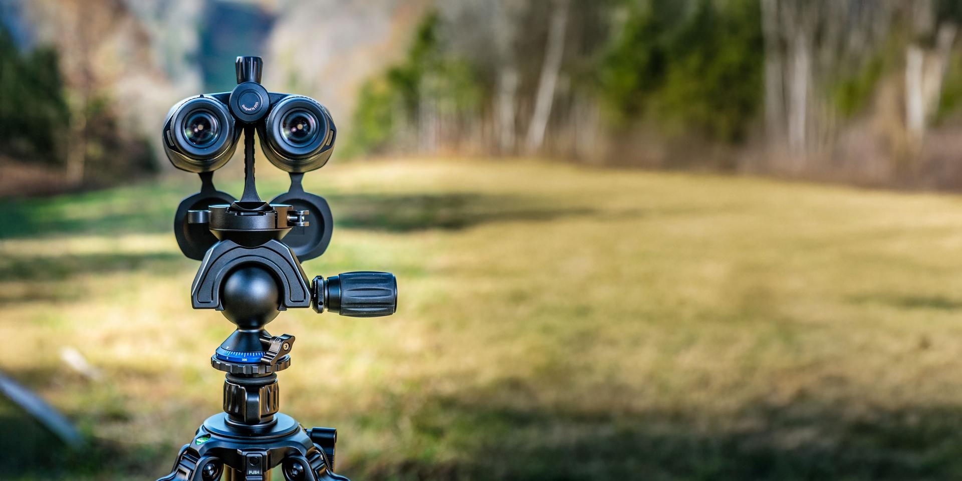High-precision ZEISS camera equipment mounted on a tripod set up in an open grassy field with a forest in the background.