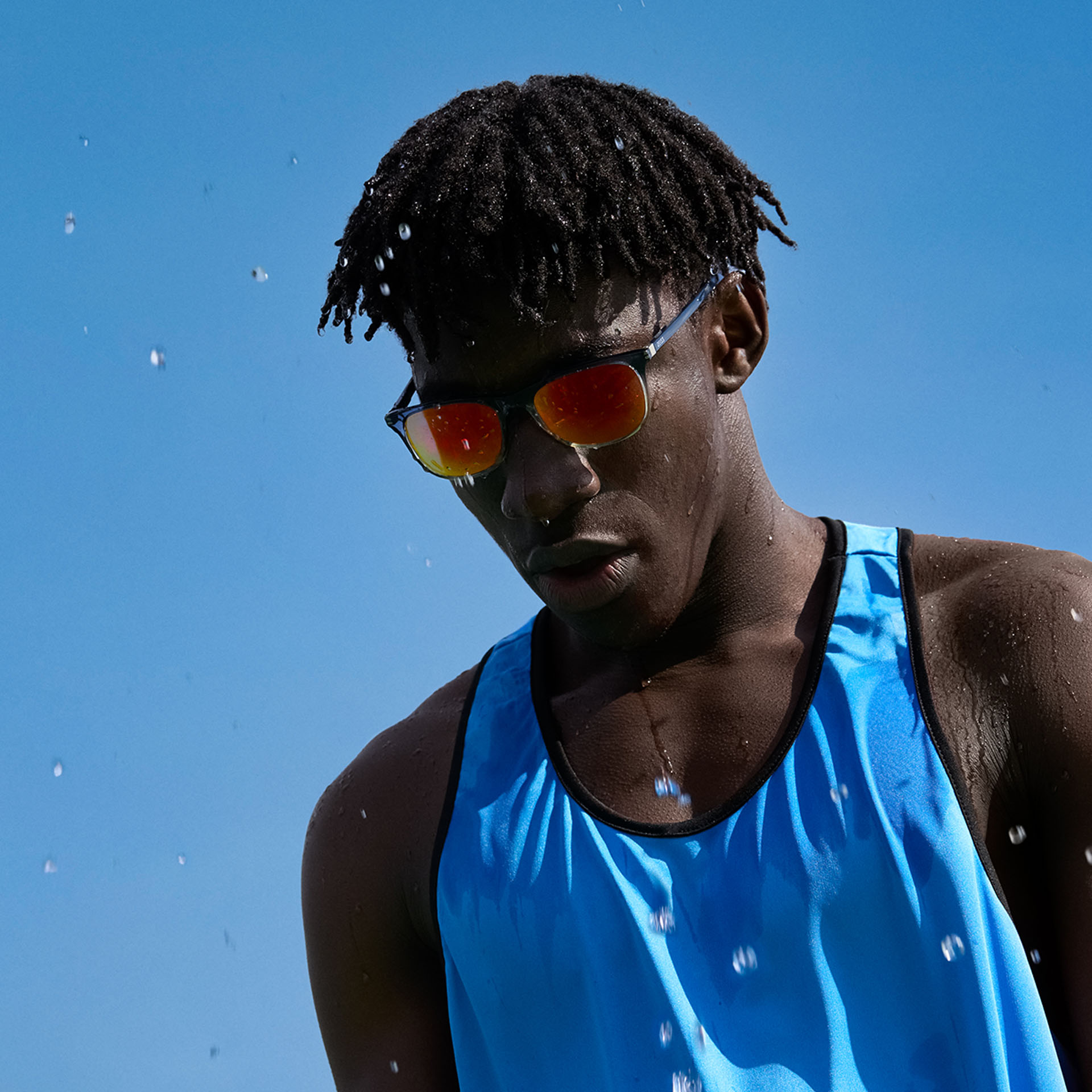 Un giovane uomo indossa occhiali sportivi e le lenti per occhiali da sole ZEISS Performance nella tonalità marrone-arancione di fronte a un cielo blu.
