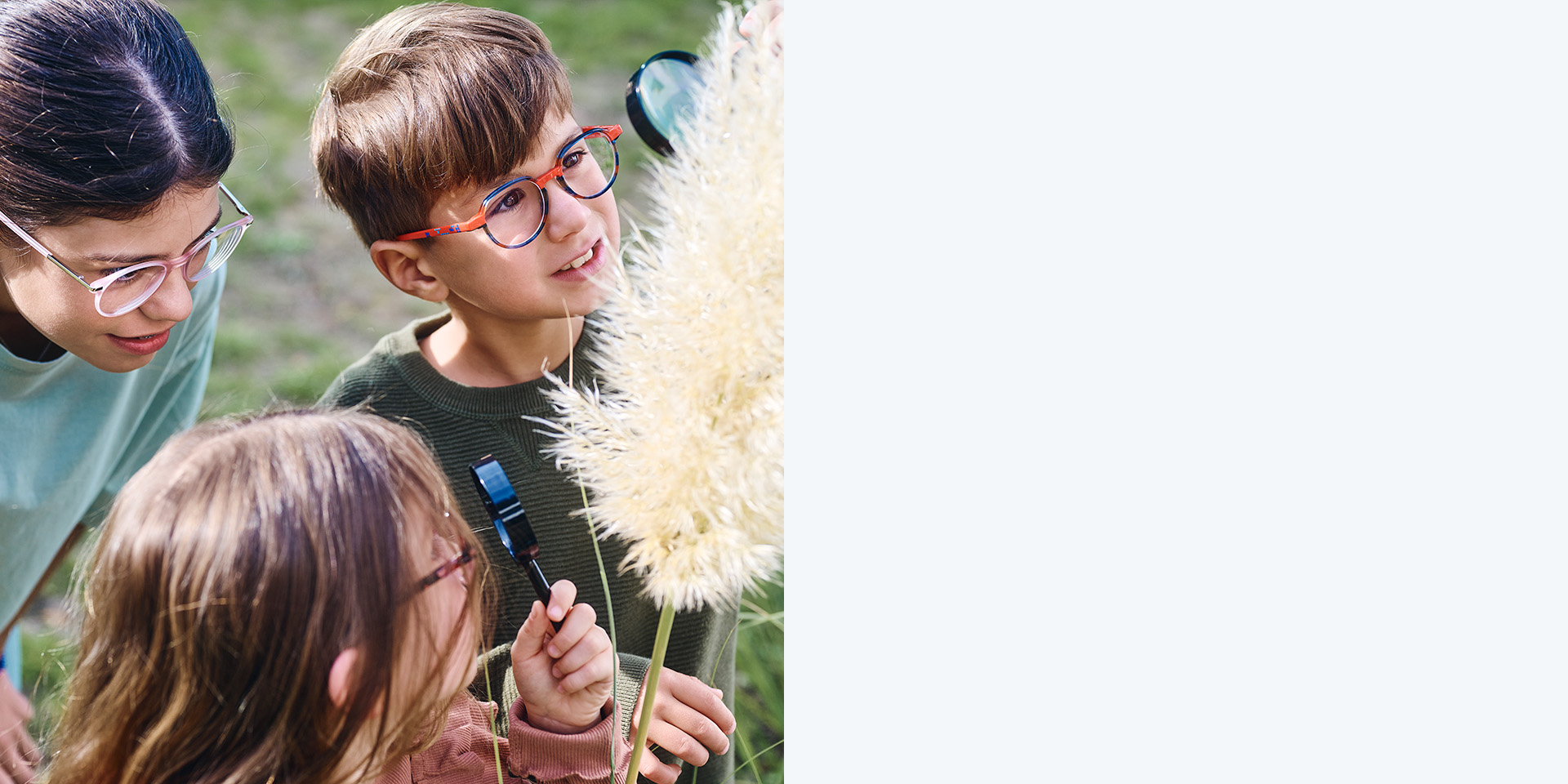 Due bambine e un bambino che indossano le lenti ZEISS MyoCare. Guardano una pianta, due dei tre bambini osservano una pianta attraverso una lente d’ingrandimento.