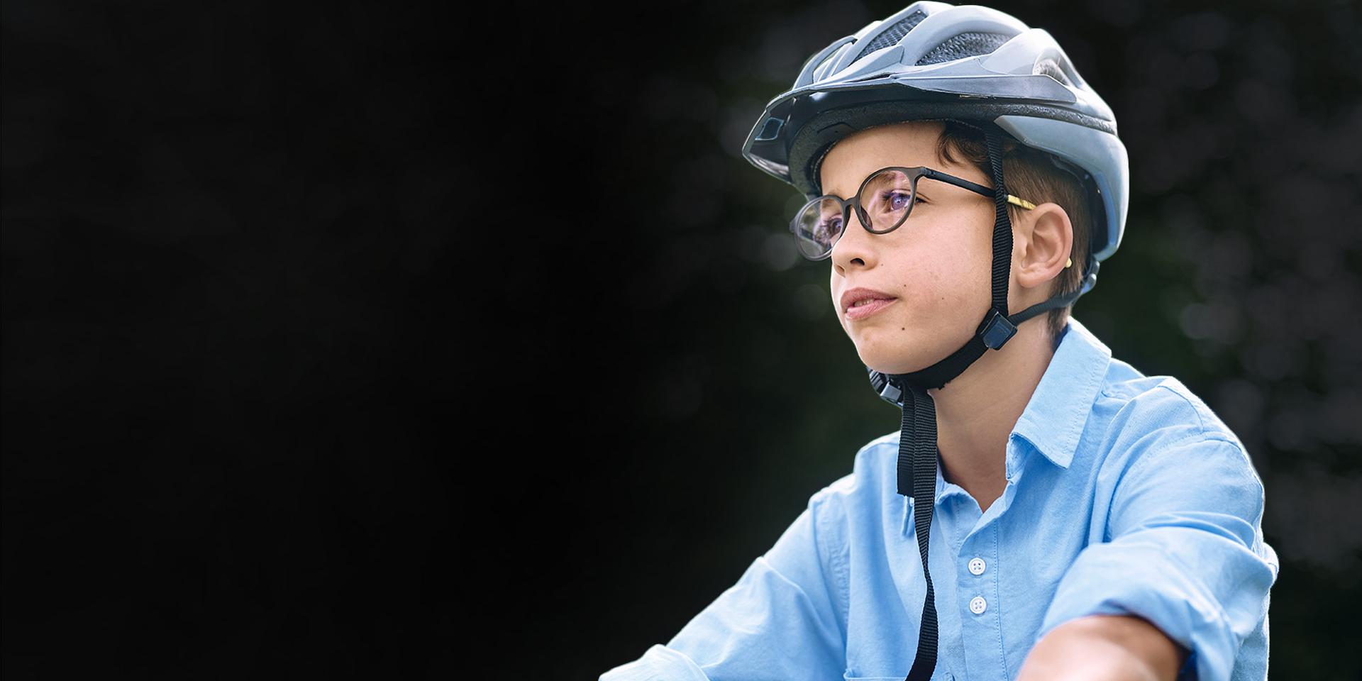 Un bambino in sella a una bicicletta con gli occhiali e un casco.