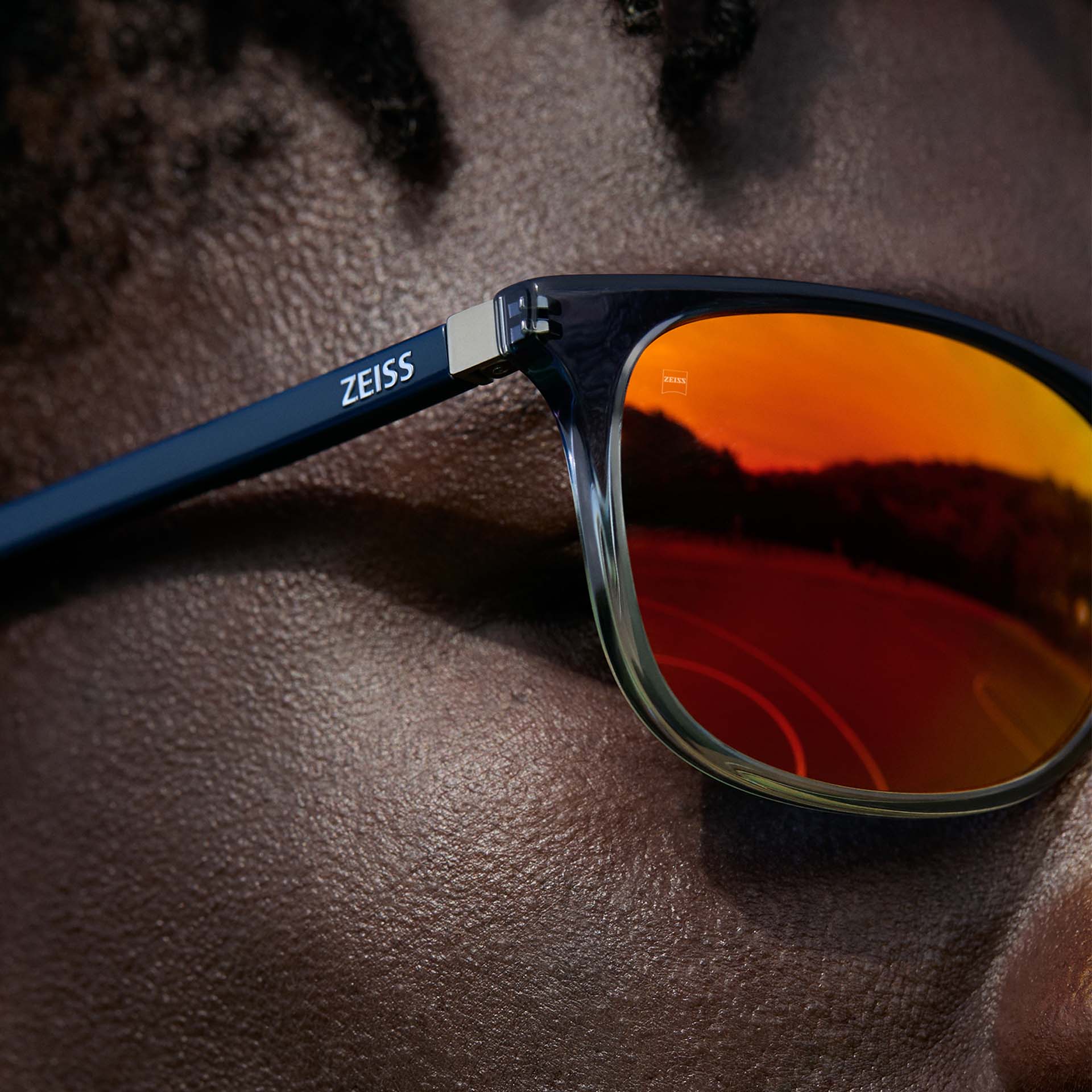 Primo piano di un uomo che indossa occhiali ZEISS con trattamento per occhiali da sole ZEISS DuraVision Mirror UV in arancione.