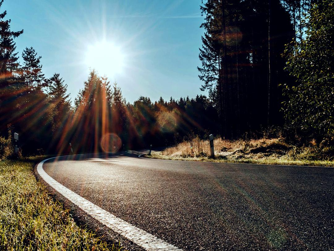 Immagine a scorrimento in cui una metà mostra una strada nel bosco con la luce intensa del sole, e l&apos;altra metà mostra la stessa strada con effetto bagliore ridotto e contrasto maggiore, enfatizzando l&apos;effetto delle lenti per occhiali da sole polarizzate.