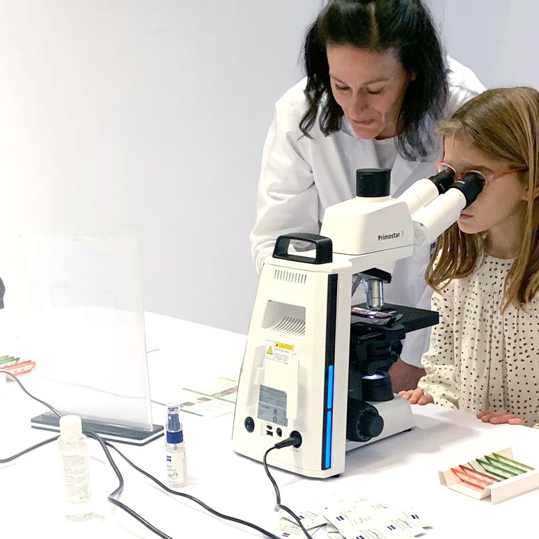 Una collaboratrice di ZEISS spiega ad una bambina delle scuole elementari come usare il microscopio