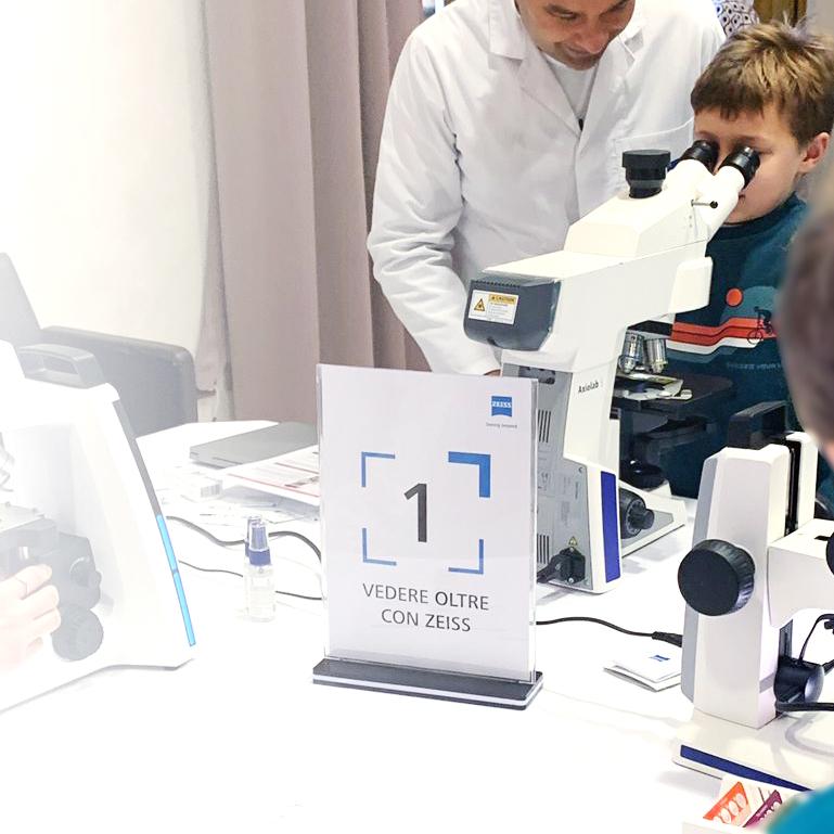 Un collaboratore di ZEISS spiega ad un bambino delle scuole elementari come usare il microscopio