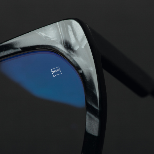 Immagine ravvicinata di una lente da occhiale in una montatura nera con logo ZEISS inciso ben visibile. 