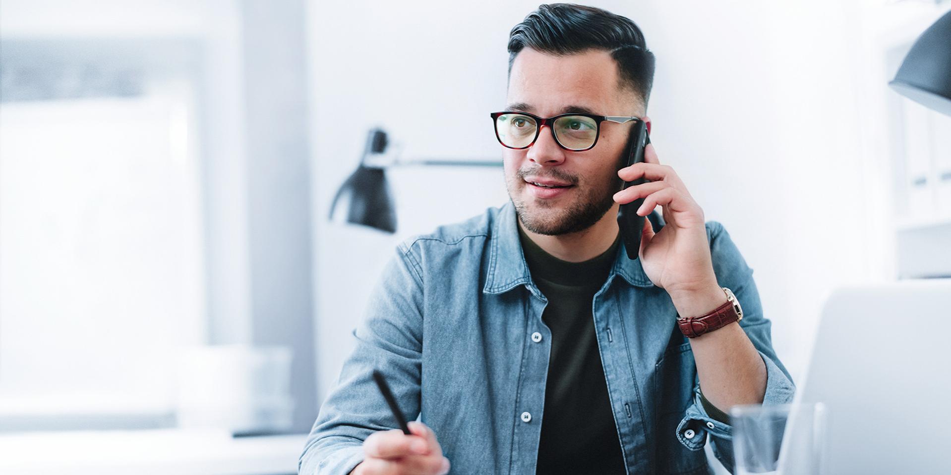 Giovane uomo al telefono mentre siede ad una scrivania in un ufficio