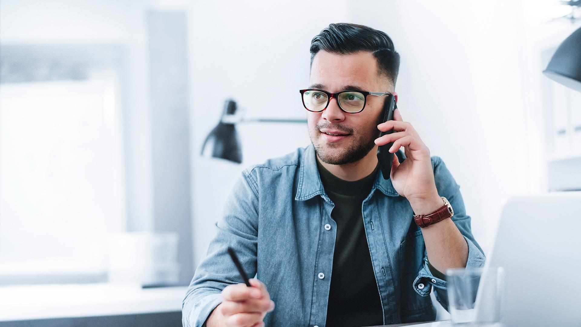 Giovane uomo al telefono mentre siede ad una scrivania in un ufficio