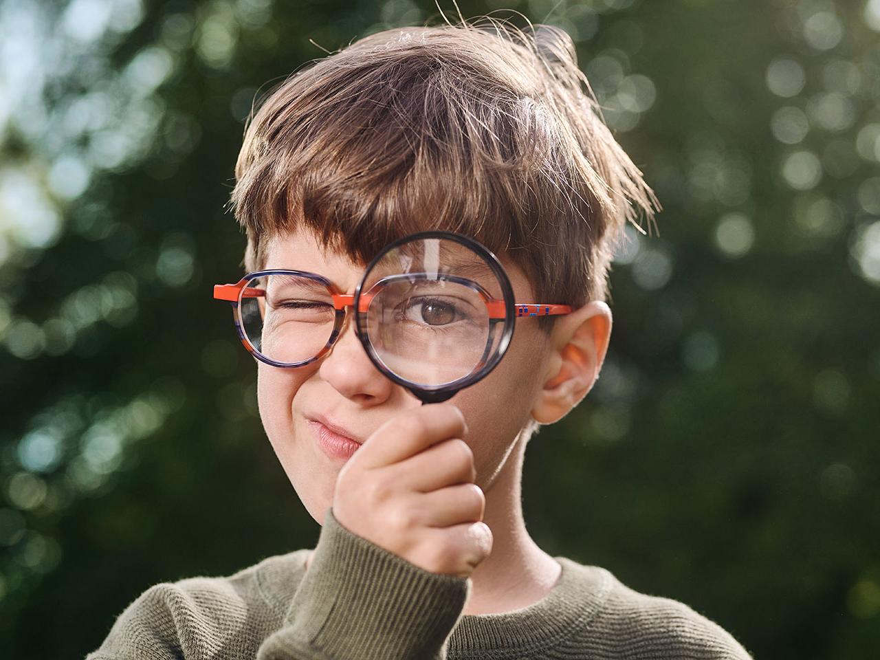 Ragazzo con gli occhiali che usa una lente di ingrandimento 