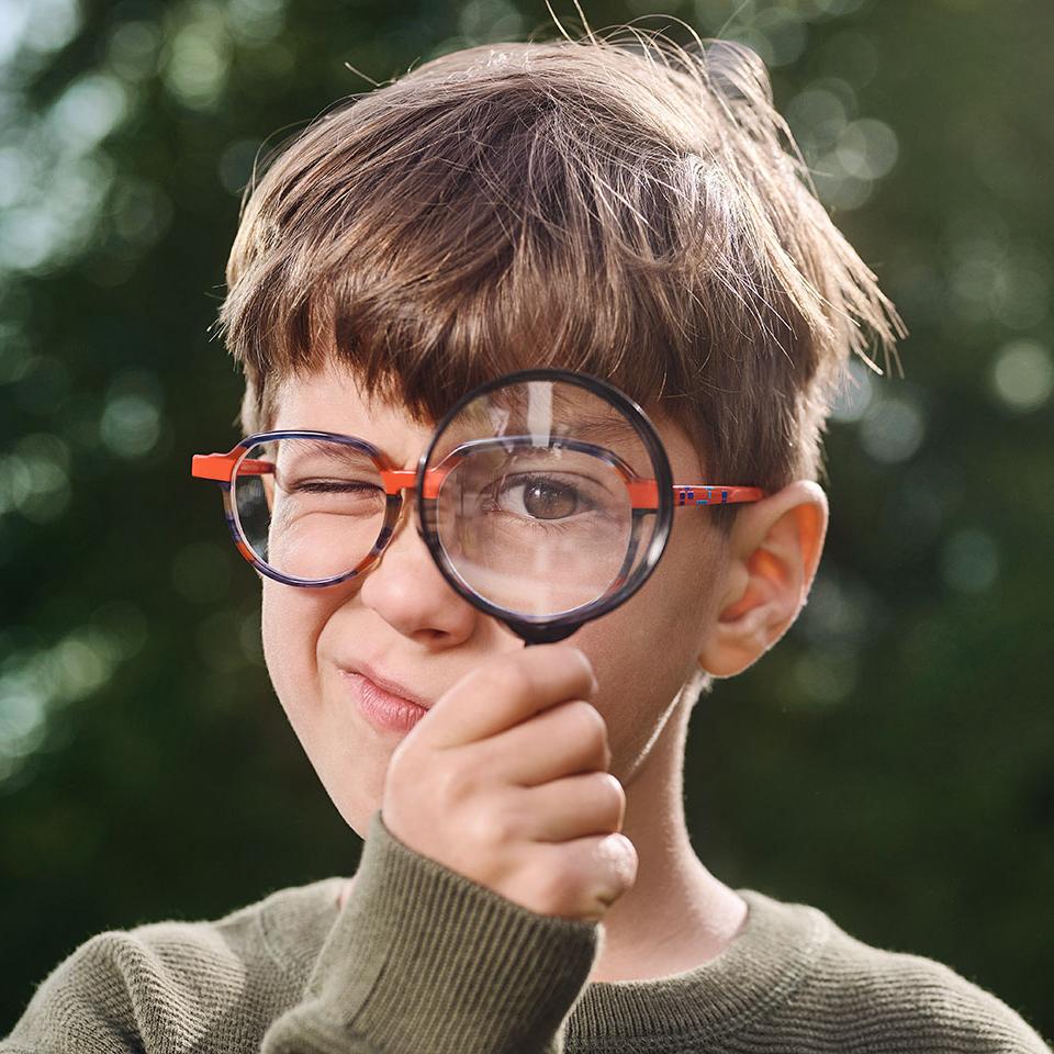 Ragazzo con gli occhiali che usa una lente di ingrandimento 