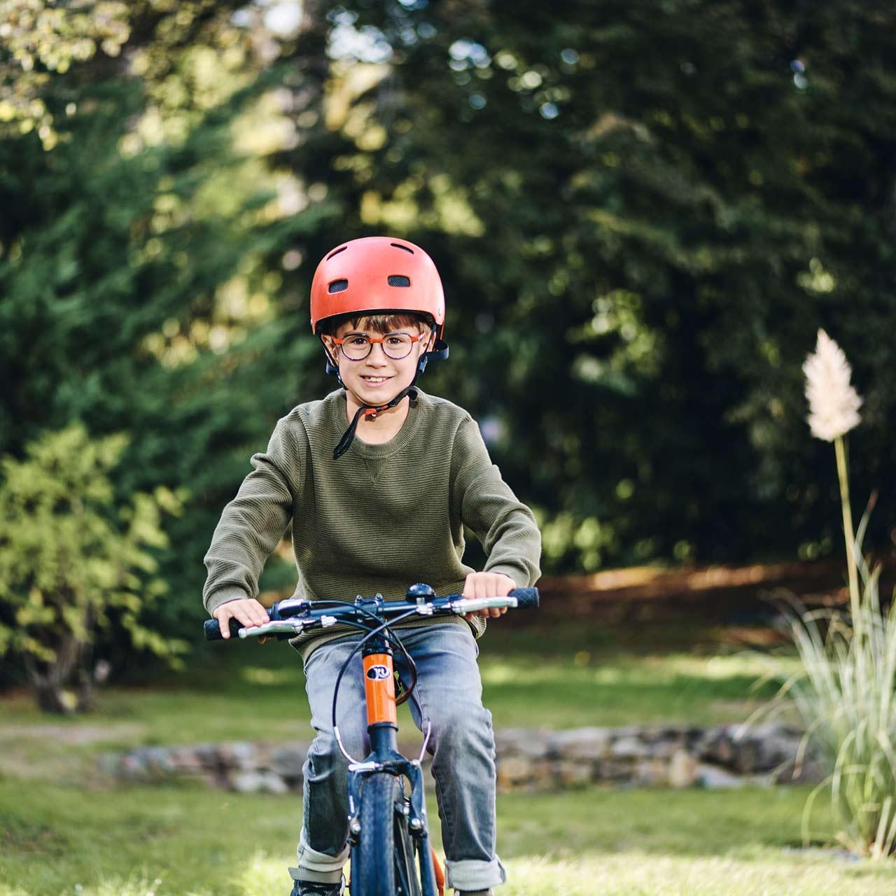 Ragazzo con occhiali che va in bici all'aperto e sorride