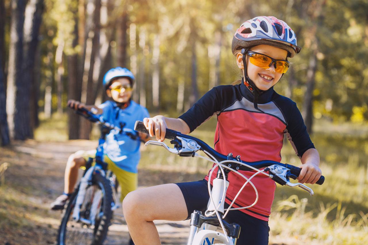 Bambini in bicicletta nel bosco assolato. Bambini in bicicletta all&apos;aperto con il casco