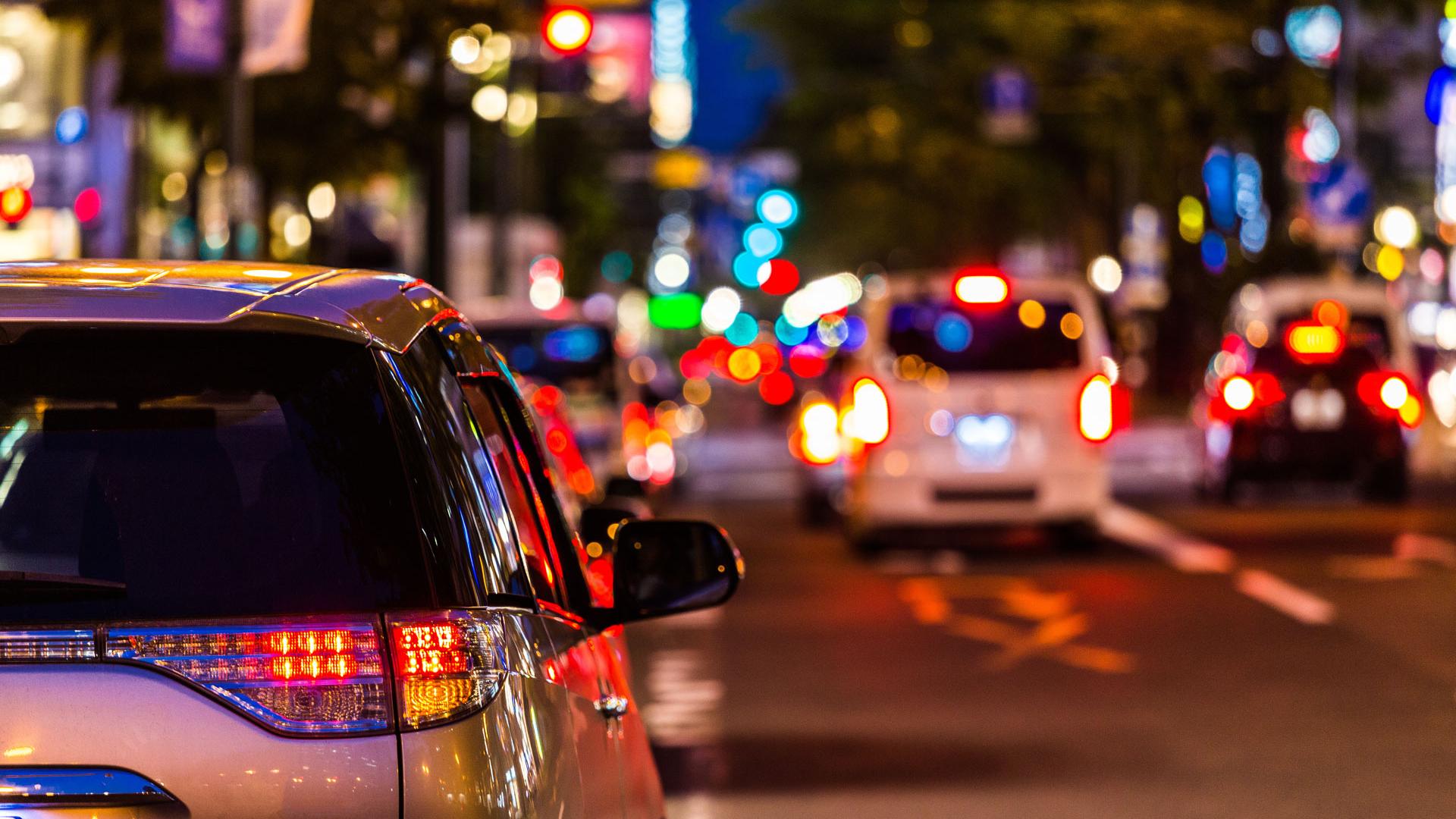 Vista posteriore di un'auto ferma a un semaforo in città di notte con luci sfocate sullo sfondo.