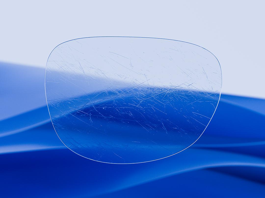 Immagine divisa che mostra una lente ZEISS su una metà, caratterizzata da chiarezza e pulizia, mentre l'altra metà mostra una lente convenzionale graffiata, evidenziando il contrasto nella durata. 