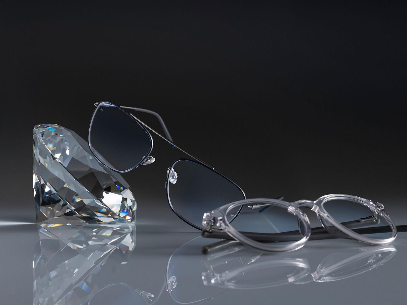 Due paia di occhiali con lenti ZEISS dotate del trattamento ZEISS più resistente di sempre: DuraVision® Platinum. Un paio di occhiali è appoggiato a un cristallo, l&apos;altro giace a terra. Entrambi hanno lenti trasparenti senza riflessi bluastri.