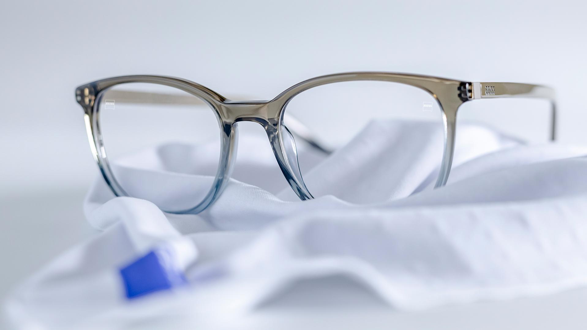 Un paio di occhiali con montatura grigio-blu e lenti ZEISS con trattamento DuraVision® posato su un panno in microfibra bianco.