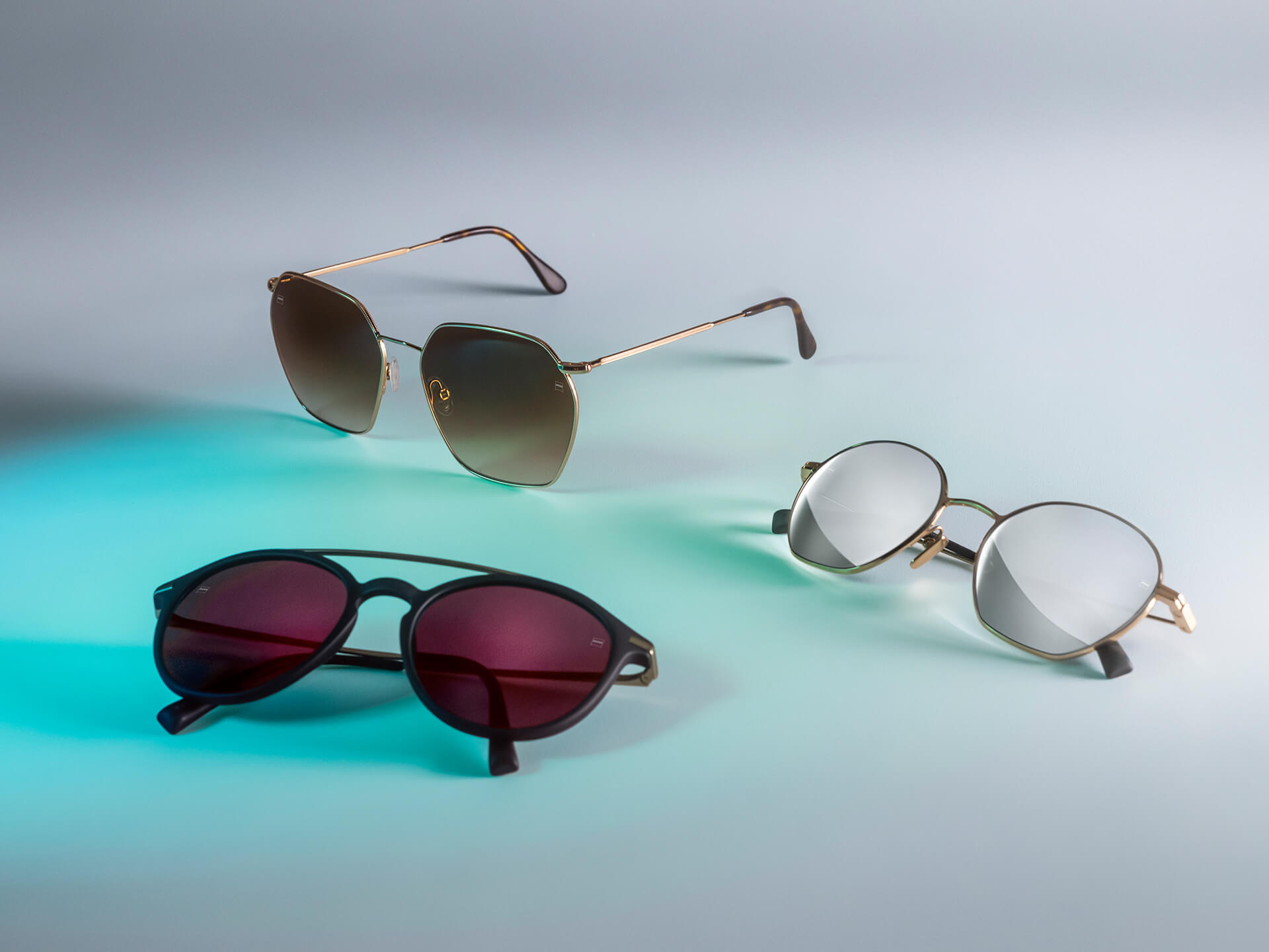 Tre paia di occhiali da sole con lenti ZEISS di colore diverso, dotate dei trattamenti DuraVision Sun, DuraVision Mirror e Flash Mirror, visibili su uno sfondo bianco con un riflesso di luce blu.