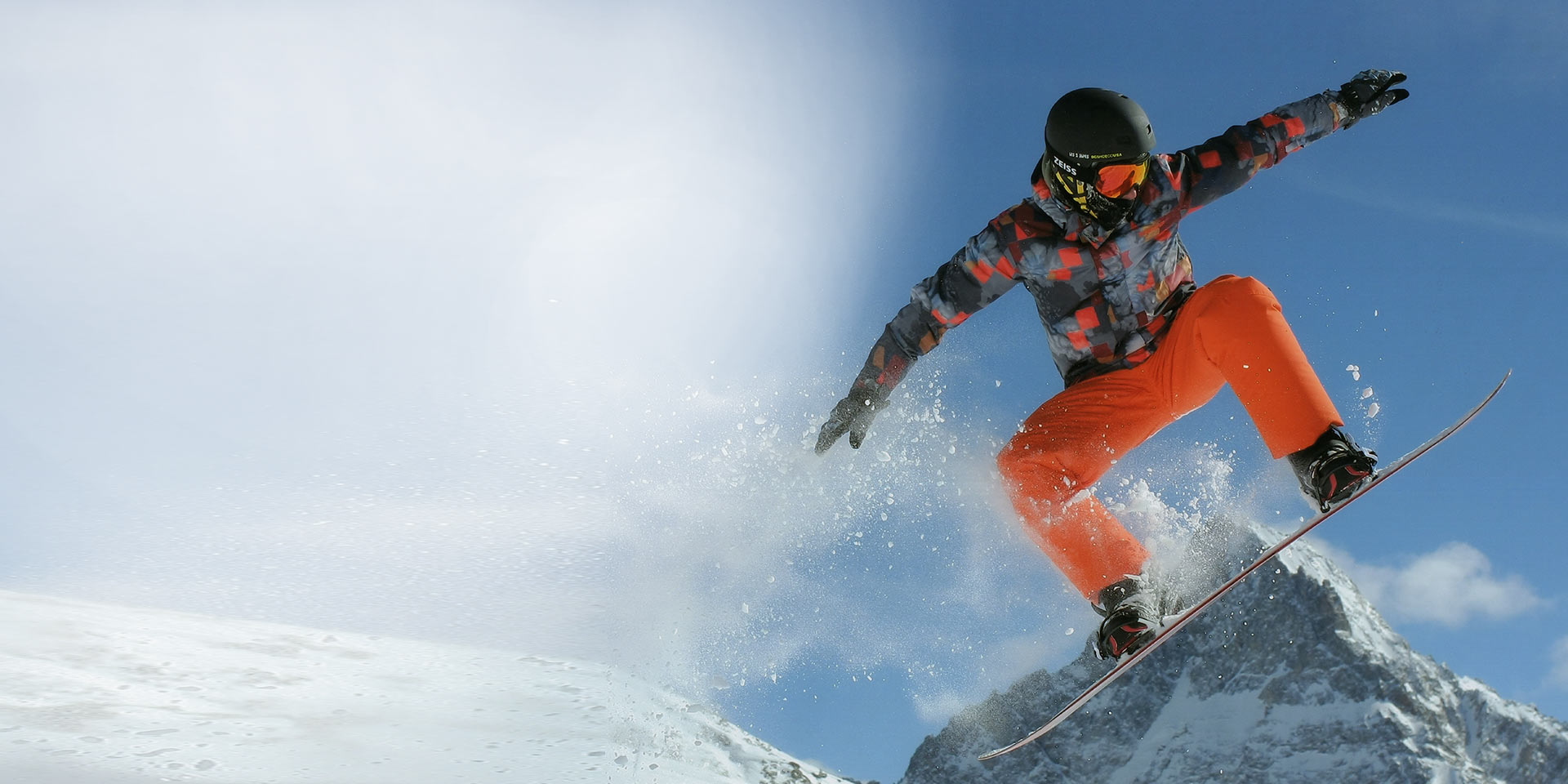 Un uomo salta con lo snowboard, indossa un casco da sci nero e una maschera da sci ZEISS con tecnologia Interchargeable per maggiore protezione