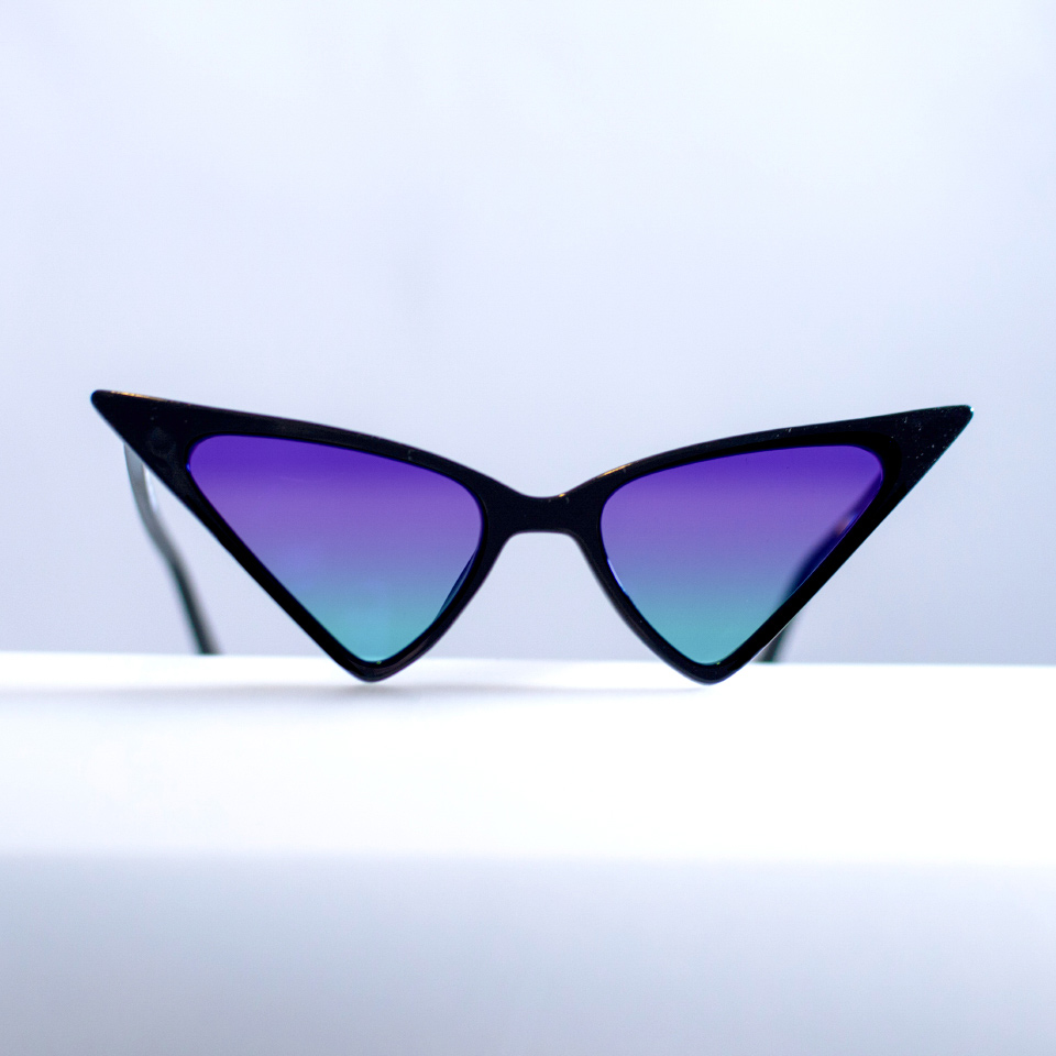 Straordinari occhiali da sole a occhi di gatto su una superficie bianca con sfumature ciano-viola