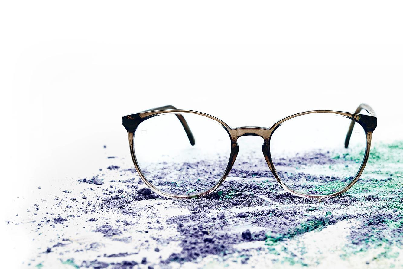 Un paio di occhiali con lenti chiare su della polvere colorata.