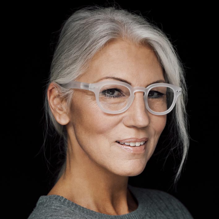 Donna con capelli grigi che porta lenti progressive SmartLife di ZEISS con una montatura bianca. Scansione geometrica del viso che mostra le misurazioni dell'anatomia facciale e della montatura.