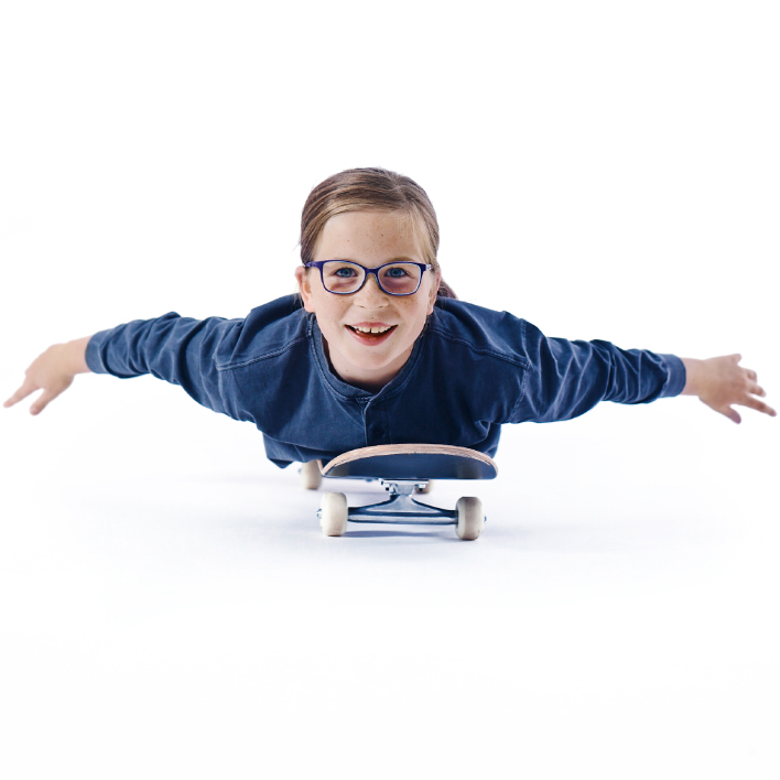 Una ragazzina con gli occhiali distesa su uno skateboard.
